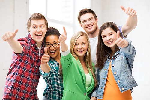 Fröhliche, junge Menschen schauen in die Kamera und strecken ihre Daumen nach oben.